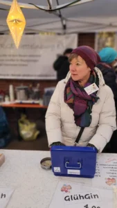 Eine Person sitzt an einem Tisch eines Marktstandes der ARGE und hat vor sich eine geöffnete und blaue Geldkassette.