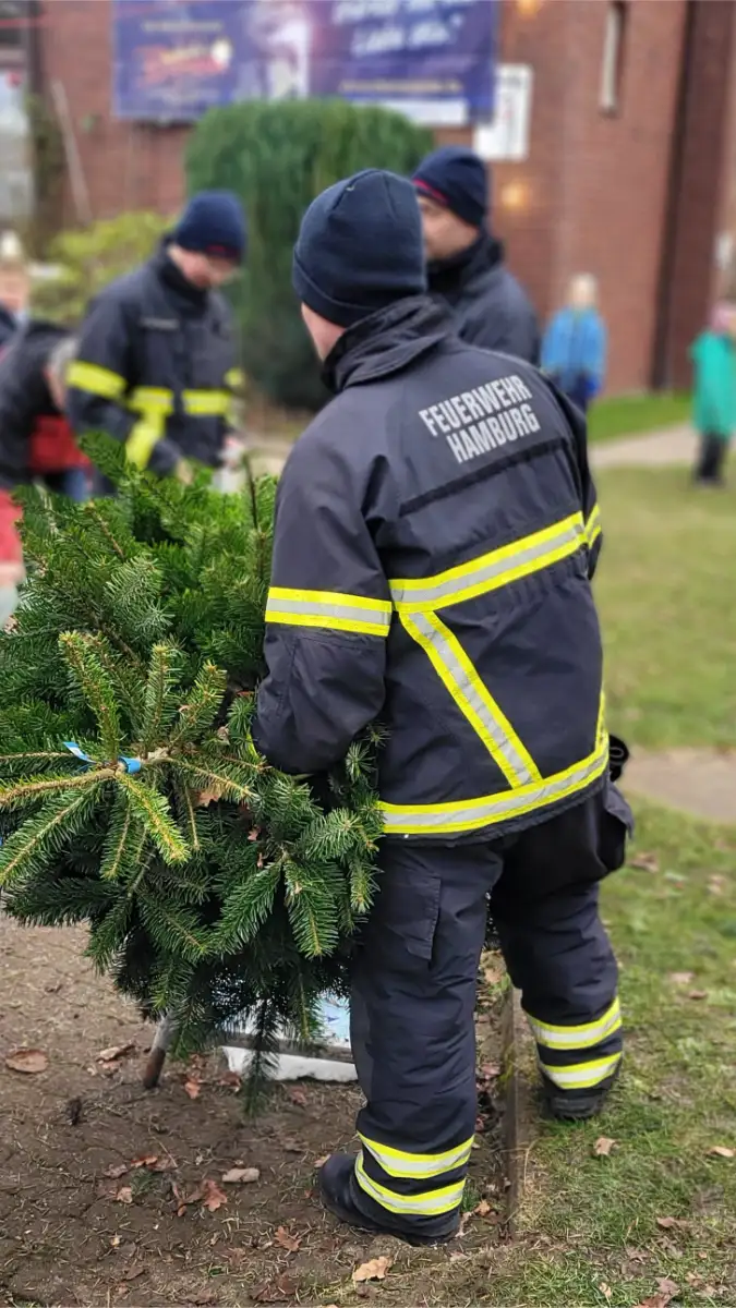 Eine Person in Feuerwehruniform hält einen Tannenbaum in den Händen.