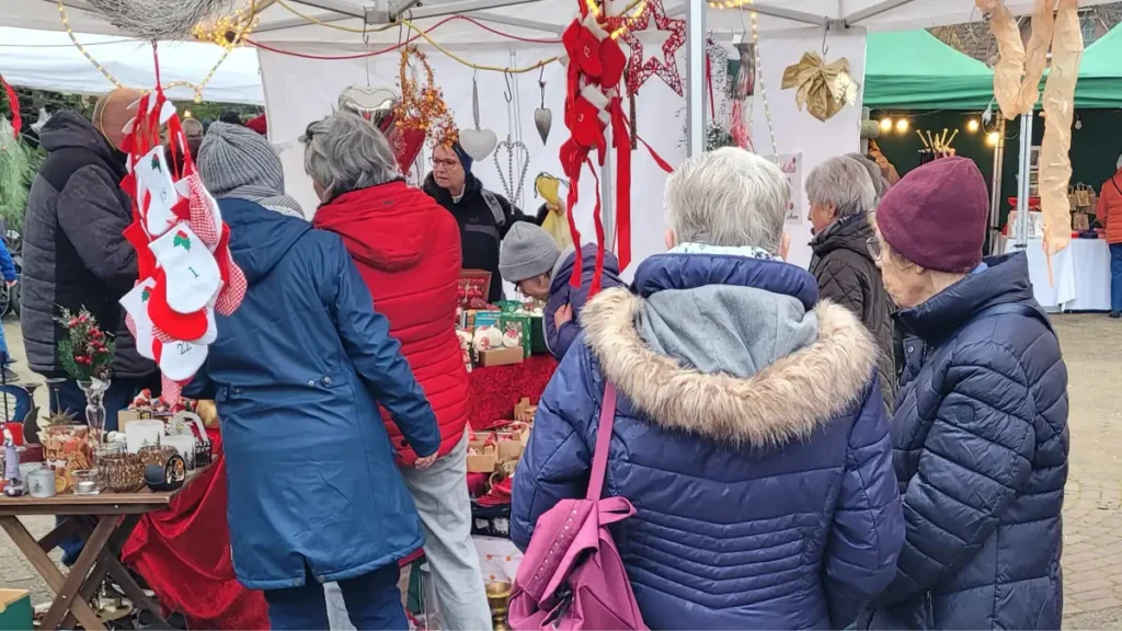 Mehrere Personen, die meisten sind von hinten zu sehen, tummeln sich an Marktständen auf dem Weihnachtsmarkt.