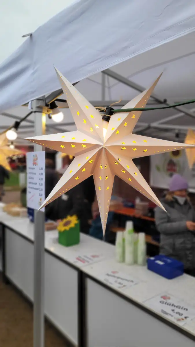 Ein leuchtender Weihnachtsstern hängt an einer Weihnachtsmarktbude.